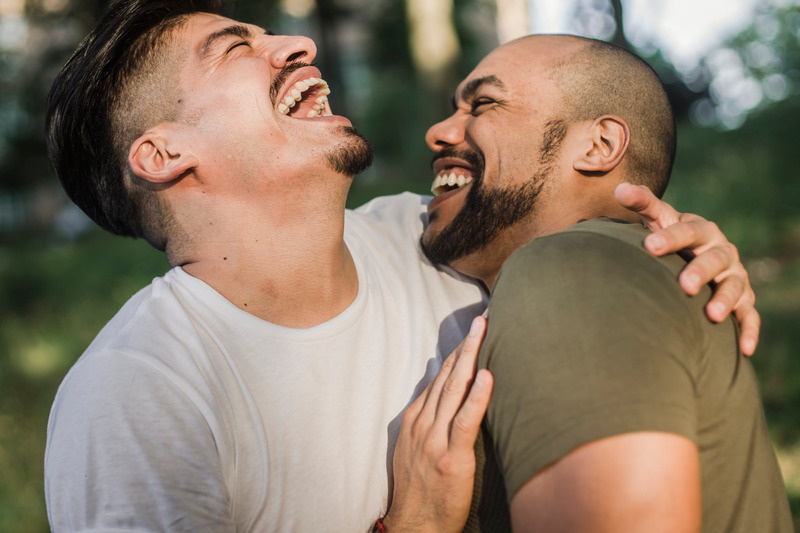 Two men with rainbow face paint, foreheads close in tender connection